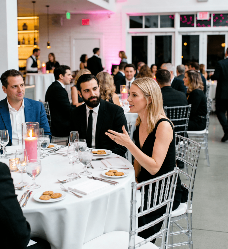 Guests seated at a formal event with pink lighting, round tables, and contemporary décor in a modern venue.